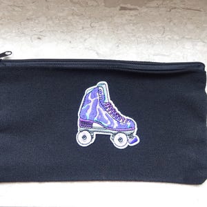 May include: A black canvas zippered pouch with a colorful embroidered roller skate patch. The roller skate design features shades of purple, blue, and white. The pouch is rectangular and has a black zipper.