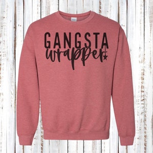Könnte beinhalten: Ein rot-oranges Sweatshirt mit Rundhalsausschnitt und dem schwarzen Aufdruck "GANSTA wrapper". Der Text hat eine Stern-Grafik. Das Sweatshirt besteht aus einem weichen Material.