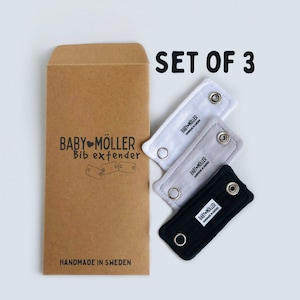 Pode incluir: Conjunto de três extensores de babador cinzentos, brancos e pretos com o texto "BABY MÖLLER HANDMADE IN SWEDEN" em cada extensor. Os extensores são embalados em um envelope marrom com o texto "BABY MÖLLER Bib extender HANDMADE IN SWEDEN" impresso na frente.