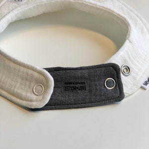 May include: White and gray baby bib with a snap closure and the text "BABY+MOJITO" printed on the gray fabric.