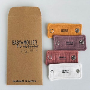 May include: A brown paper envelope labeled BABY MÖLLER Bib extender and four rectangular fabric bib extenders in mustard yellow, mauve, dusty rose, and white. Each fabric piece features two metal snap buttons and the BABY MÖLLER logo printed in black.