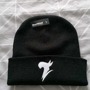 Puede incluir: Gorro negro con un logotipo blanco estilizado del número 7 en la parte delantera. El gorro tiene un dobladillo abatible y una etiqueta que dice "Beechfield Original Headwear".