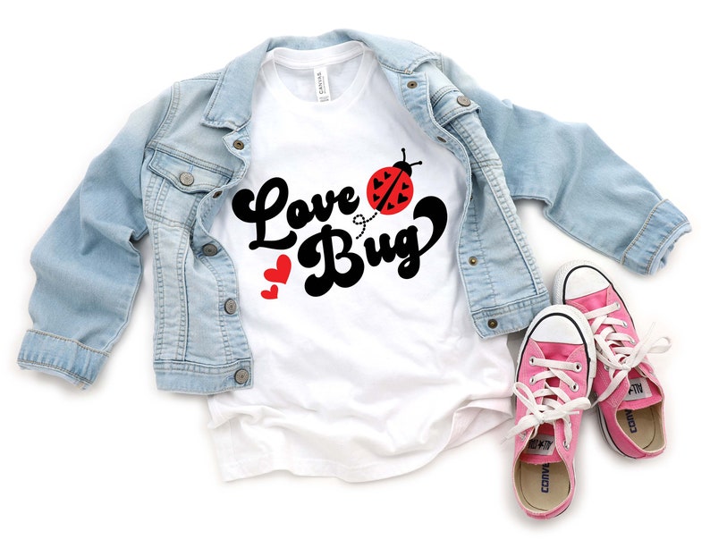 May include: A white t-shirt with the words "Love Bug" in black script, a red ladybug graphic, and two red hearts. A light blue denim jacket and pink sneakers with white laces complete the ensemble.