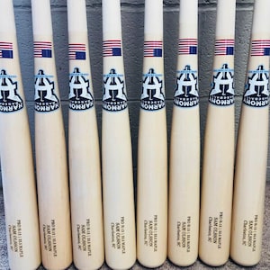 May include: Ten wooden baseball bats with a white and blue baseball logo and the text "Harmony Baseball" on each bat. The bats are labelled with "PRO H-13 | 33.5 MAPLE SAM OLSSON Charleston, SC".