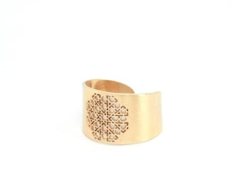 Könnte beinhalten: Ein goldfarbenes Metall-Armband mit einem ausgeschnittenen geometrischen Muster in der Mitte.