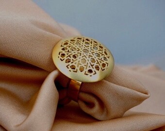 Könnte beinhalten: Ein goldener Ring mit einem runden Design, das ein geometrisches Muster zeigt. Der Ring liegt auf einem braunen Stoffhintergrund.