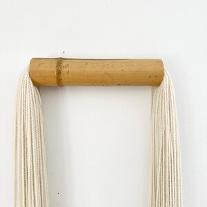 Neutral tassel wall decor made of cotton and bamboo hanging above sofa in modern living room, minimalist home styling