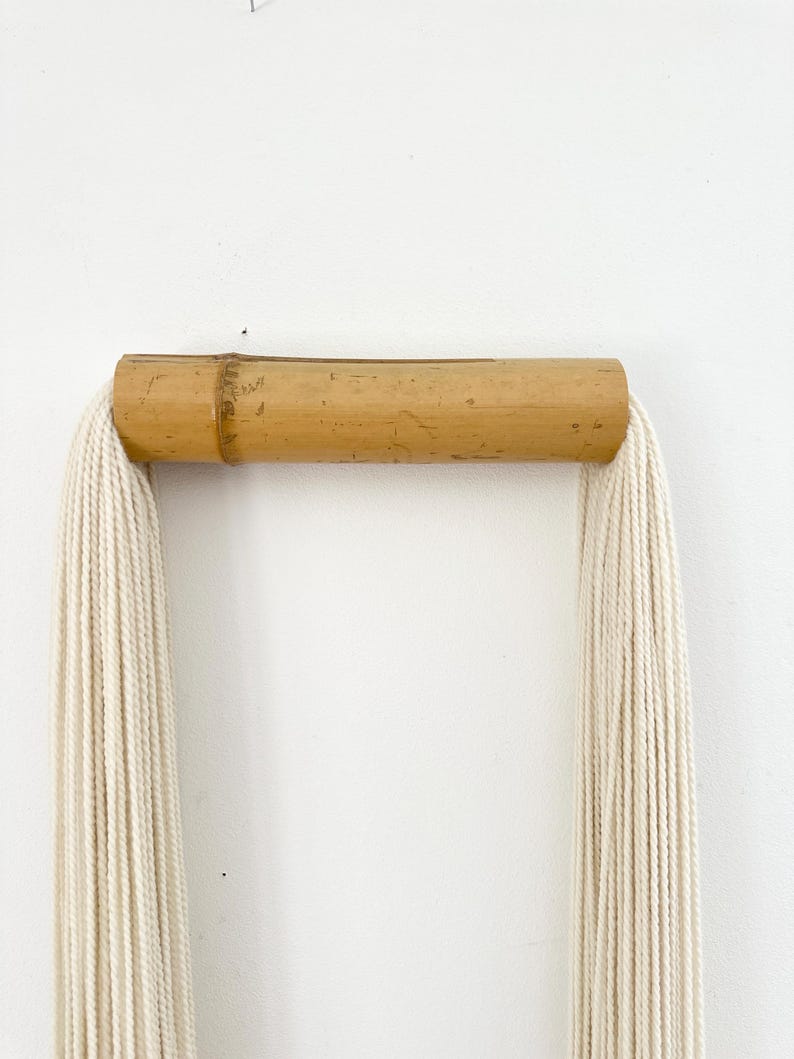 Neutral tassel wall decor made of cotton and bamboo hanging above sofa in modern living room, minimalist home styling