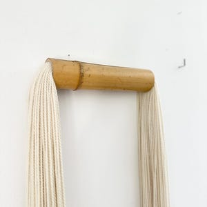 Handmade tassel wall hanging displayed above wooden console, soft neutral decor, Scandinavian style interior