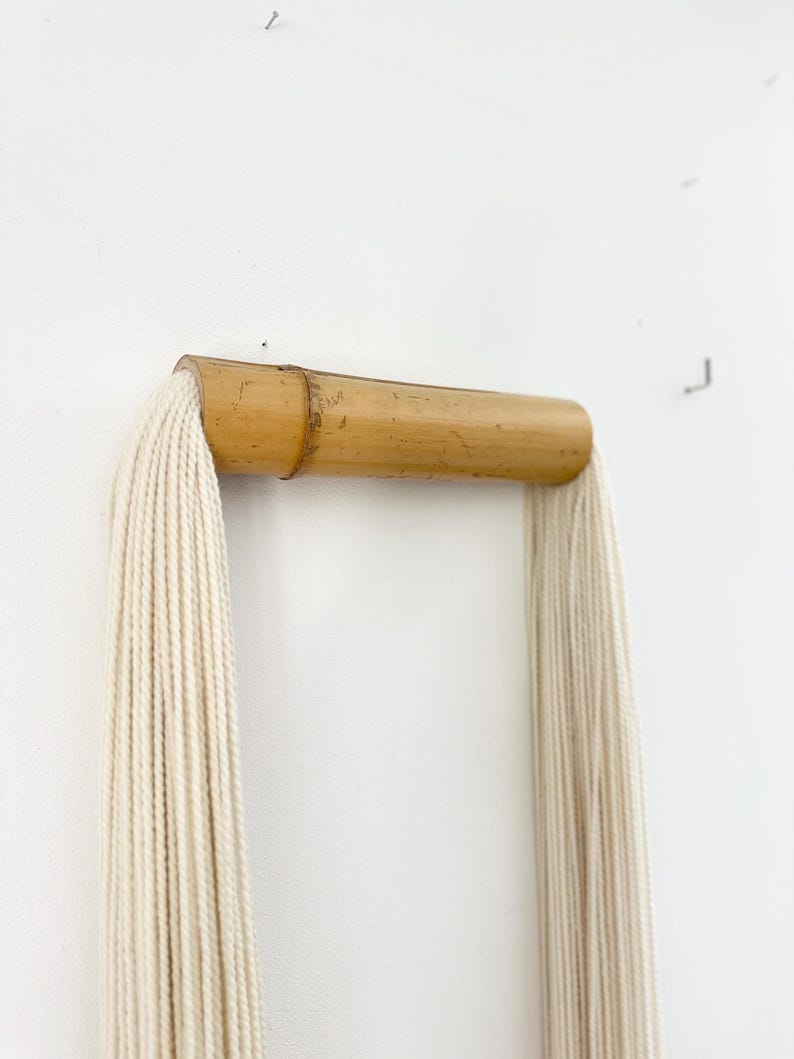 Handmade tassel wall hanging displayed above wooden console, soft neutral decor, Scandinavian style interior