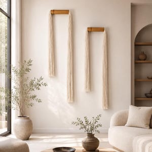 Minimalist tassel wall hanging made of natural cotton and bamboo displayed on a dark charcoal wall above a wooden console in a modern living room, neutral decor, organic modern styl