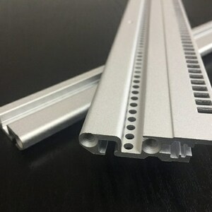 May include: Two pieces of silver aluminum extrusion with a series of holes and slots along the edge. The extrusion is used for building and construction.