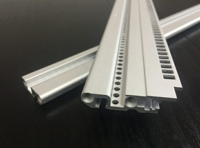 May include: Two pieces of silver aluminum extrusion with a series of holes and slots along the edge. The extrusion is used for building and construction.