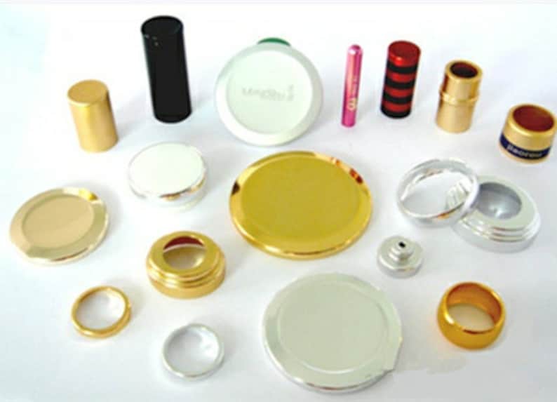 May include: Assortment of gold, silver, and black metal bottle caps and lids. Some caps have a raised rim, while others are flat. There are also a few small, round, metal rings.