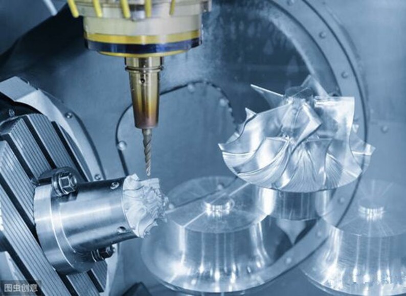 May include: A close-up of a CNC machine cutting a metal part. The machine has a drill bit attached to a robotic arm, and the part is being held in a vise. The machine is in a factory setting.