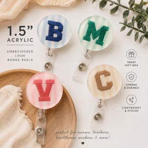 May include: Four 1.5 inch round acrylic badge reels with embroidered letters B, M, V, and C. Each reel features a pastel striped background in blue, green, pink, or beige. The badge reels include a clear plastic strap and a metal snap button closure.