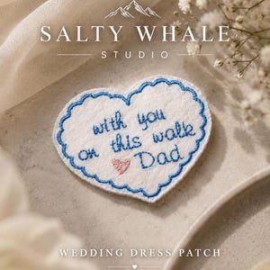 May include: A white heart-shaped fabric patch with a scalloped blue embroidered edge. The text "with you on this walk Dad" is embroidered in blue thread, accompanied by a small pink embroidered heart in the center of the patch.