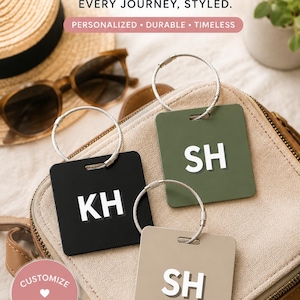 May include: Three square luggage tags in black, olive green, and beige, each featuring white embossed initials KH or SH. Each tag includes a silver-toned metal cable loop for attachment. The text THE LUGGAGE TAG BEST SELLER EVERY JOURNEY, STYLED. is visible.