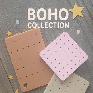 May include: The image displays three earring display cards in shades of tan, pink, and light green, each with multiple holes. The cards are arranged on a gray wooden surface, with the words "BOHO COLLECTION" in white. Decorative stars and circles are scattered around.