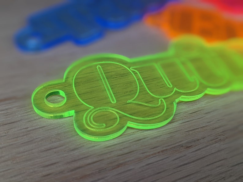 May include: A bright green acrylic keychain with the word "QUW" in a stylized font.