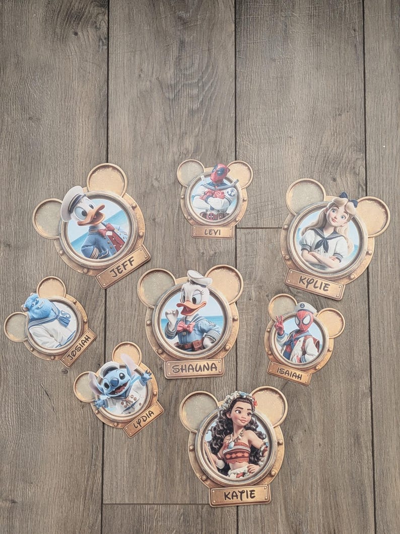 K&ouml;nnte beinhalten: Eine Sammlung von acht runden Wandplaketten in Form von Mickey-Maus-Ohren, die jeweils eine andere Figur in einem Bullaugenrahmen zeigen. Die Figuren umfassen Donald Duck, Deadpool, Alice, Sulley, Daisy Duck, Spider-Man, Stitch und Moana, mit Namensschildern f&uuml;r Jeff, Levi, Kylie, Josiah, Shauna, Isaiah, Lydia und Katie.