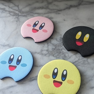 Peut inclure: Quatre dessous de verre pour voiture avec des motifs de personnages de dessins anim&eacute;s. Les dessous de verre sont roses, bleus, jaunes et noirs, chacun avec un visage souriant et un design unique. Forme circulaire avec une d&eacute;coupe.