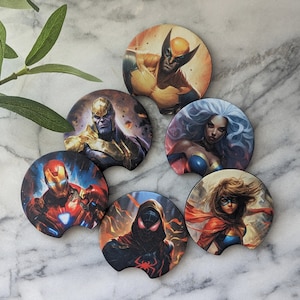May include: Six round beverage coasters featuring different comic book characters. The coasters are made of a cork-like material and have a black rubber ring around the edge. The characters featured are Wolverine, Thanos, Storm, Captain Marvel, Spider-Man, and Iron Man.