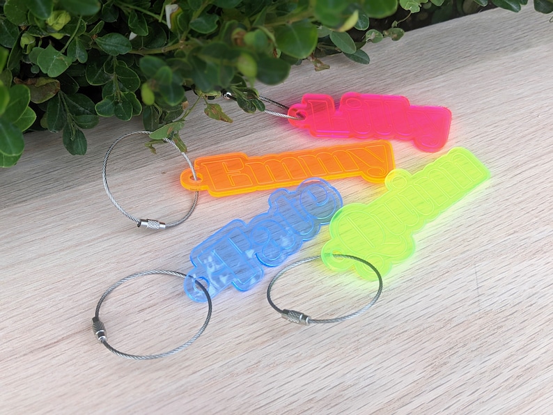 May include: Four colorful keychains with names spelled out in neon colors. The keychains are attached to silver key rings. The names are "Lilly", "Emmy", "Tracy", and "Justin".