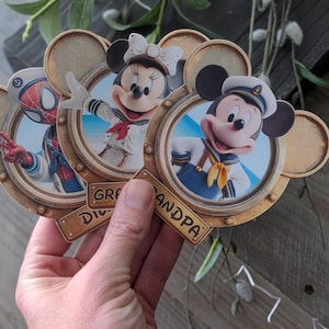 K&ouml;nnte beinhalten: Drei kreisf&ouml;rmige, goldfarbene Rahmen in Form von Mickey-Maus-Ohren, die jeweils eine Figur in nautischer Kleidung zeigen. Die Figuren sind Spider-Man, Minnie Maus und Mickey Maus. Die Rahmen haben kleine Plaketten mit der Aufschrift Grandma und Grandpa.