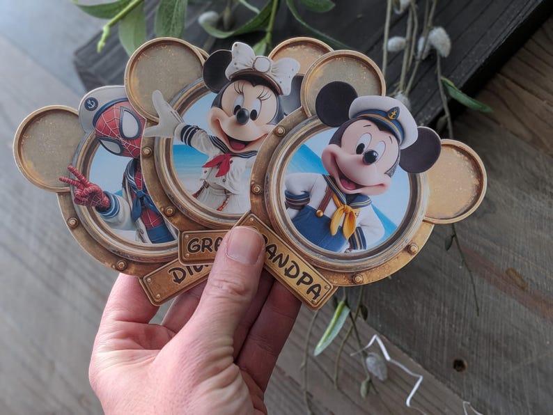 K&ouml;nnte beinhalten: Drei kreisf&ouml;rmige, goldfarbene Rahmen in Form von Mickey-Maus-Ohren, die jeweils eine Figur in nautischer Kleidung zeigen. Die Figuren sind Spider-Man, Minnie Maus und Mickey Maus. Die Rahmen haben kleine Plaketten mit der Aufschrift Grandma und Grandpa.
