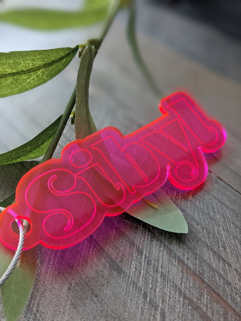 May include: A bright pink acrylic keychain with the word "silly" written in a playful, rounded font.