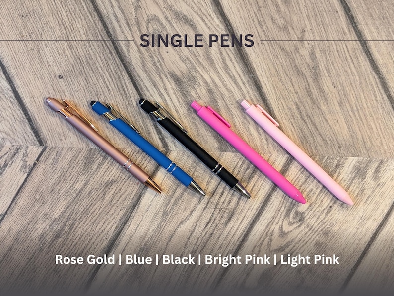 May include: Five pens on a wooden surface. The pens are rose gold, blue, black, bright pink, and light pink.  Single Pens.