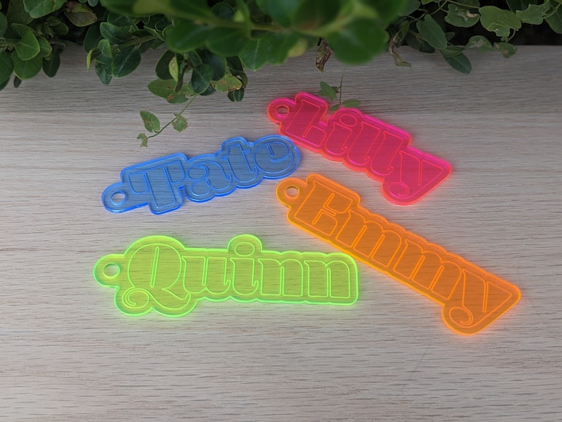 May include: Four neon-colored acrylic keychains with the names "Quinn", "Emmy", "Tate", and "Lily" in a retro font.