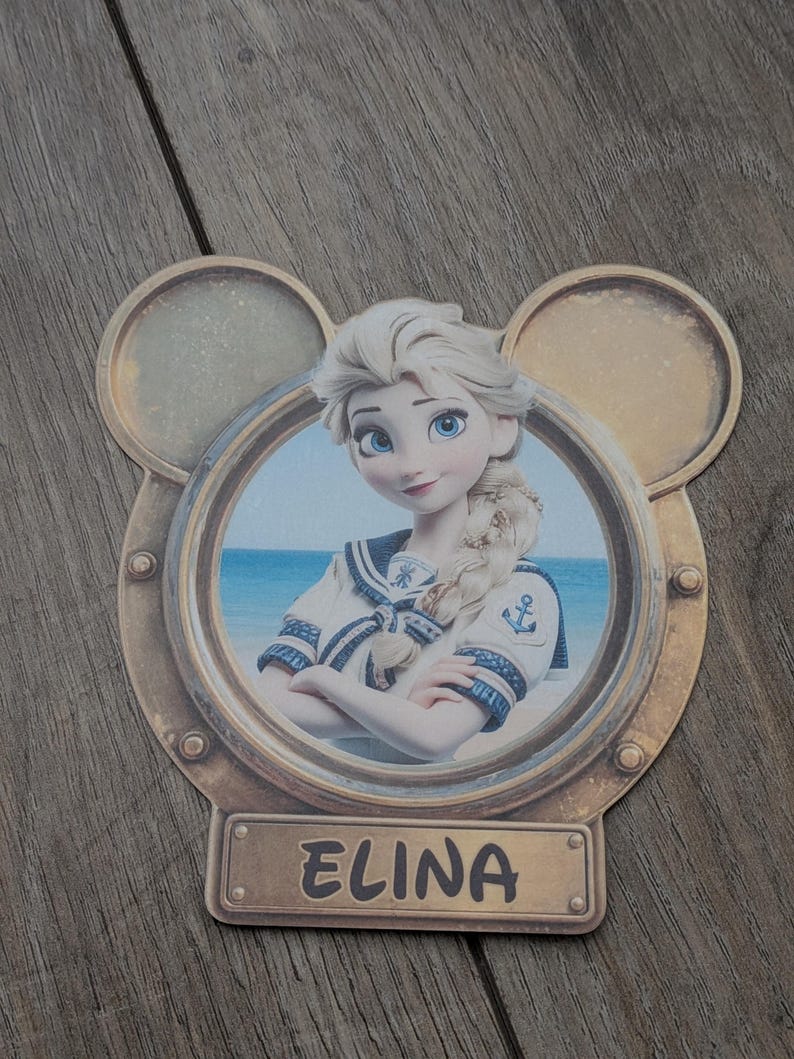 K&ouml;nnte beinhalten: Ein dekorativer Ausschnitt mit einem runden Bullaugenrahmen und Mickey-Mouse-Ohren. Im Bullauge befindet sich die Illustration einer blonden Figur in Matrosenkleidung vor einem Strandhintergrund. Ein rechteckiges Namensschild zeigt den Namen ELINA.