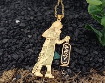 May include: Gold necklace with a pendant featuring a detailed silhouette of an Egyptian god holding a scroll with hieroglyphics. The pendant is attached to a delicate gold chain.