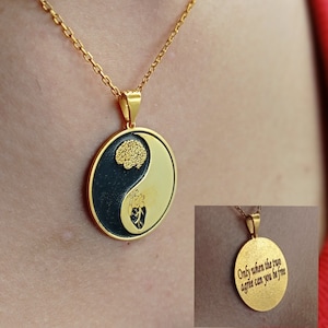 Peut inclure: Collier pendentif doré avec un design yin-yang. Un côté représente un cerveau, l'autre un cœur. Le pendentif est sur une chaîne dorée. Une petite image montre le texte : "Only when the two agree can you be free."