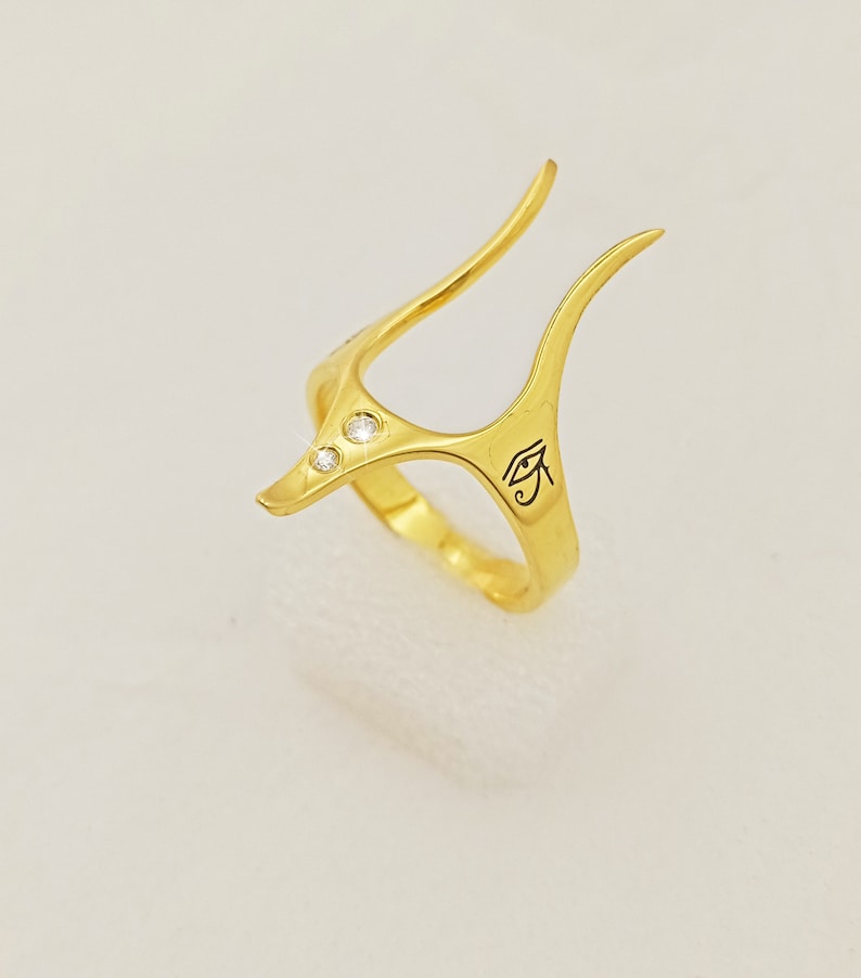 May include: Gold ring with a unique design featuring three small diamonds and an engraved Eye of Horus symbol.