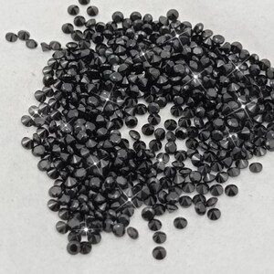 May include: A large pile of black diamond-shaped rhinestones. The rhinestones are scattered on a white surface.