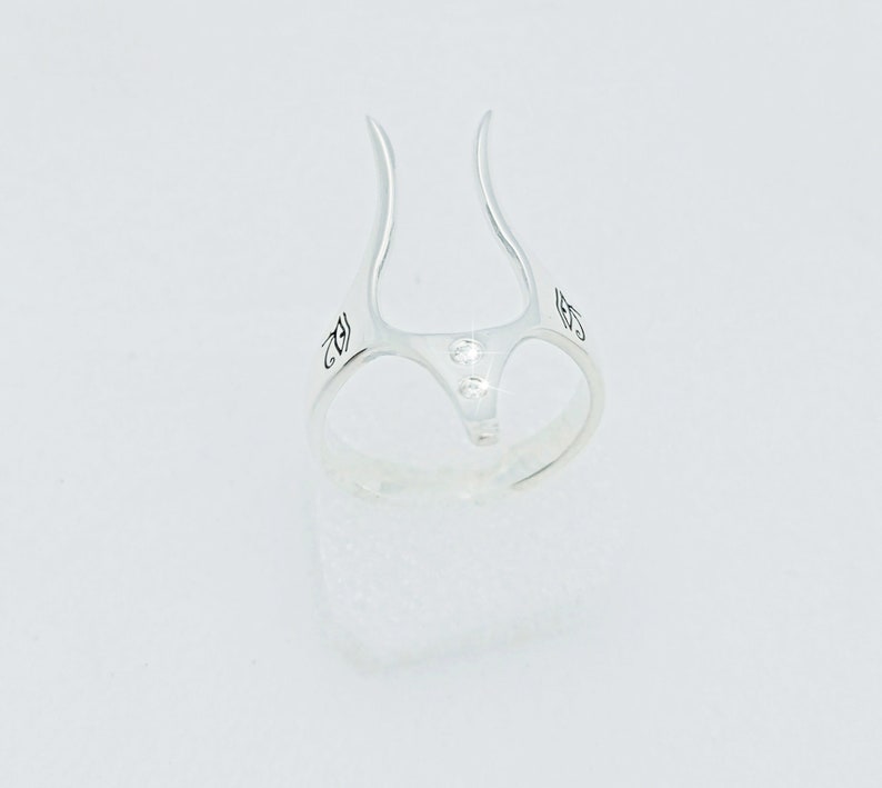 May include: Silver ring with two small clear stones set in the center. The ring has a unique design with two prongs that extend upwards.