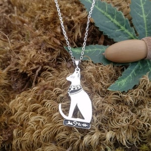 Pu&ograve; includere: Collana d'argento con un ciondolo a forma di gatto bianco con segni neri. Il gatto indossa un collare con un motivo bianco e nero. Il ciondolo ha anche geroglifici sul fondo.