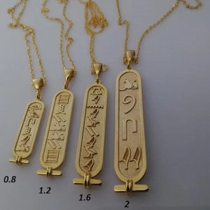 May include: Four gold necklaces with different sized pendants featuring Egyptian hieroglyphics. The pendants are 0.8 inches, 1.2 inches, 1.6 inches, and 2 inches in length.