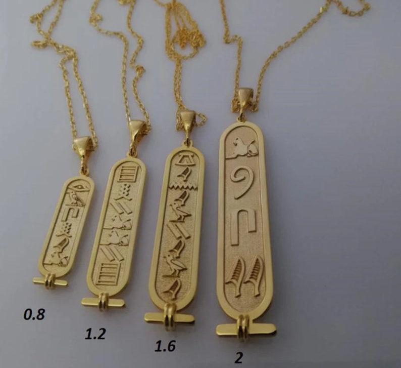 May include: Four gold necklaces with different sized pendants featuring Egyptian hieroglyphics. The pendants are 0.8 inches, 1.2 inches, 1.6 inches, and 2 inches in length.