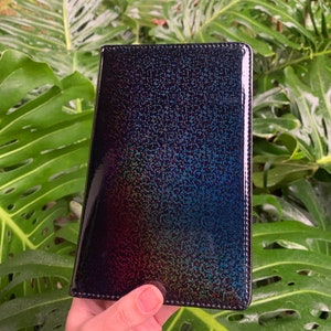 May include: A black iridescent leather wallet with a subtle sparkle. The wallet has a textured surface and a stitched edge.
