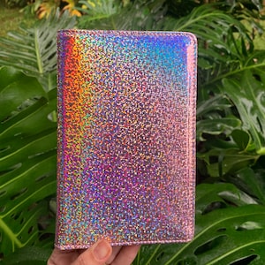 May include: A pink iridescent glitter wallet with a rainbow shimmer. The wallet is made of a soft, textured material.