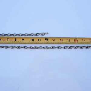 May include: Two silver chains, one measuring 25 cm and the other measuring 63.5 cm, are laid out on a white surface next to a yellow measuring tape.