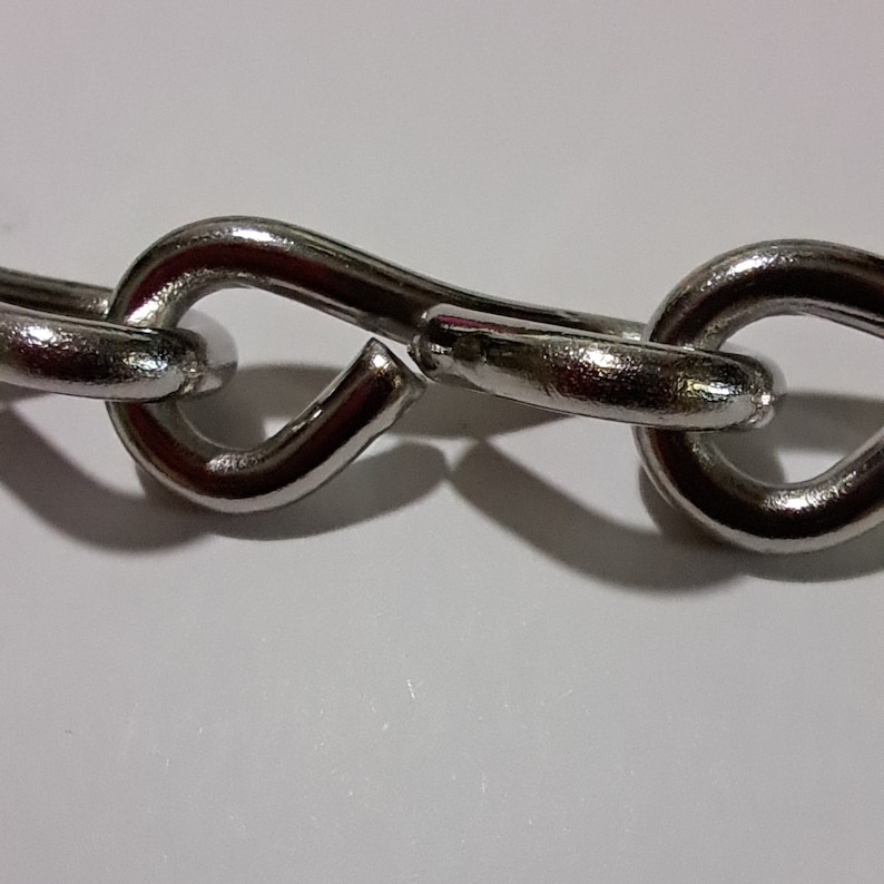 May include: A close-up of a silver chain with a broken link. The chain is made of metal and has a smooth finish.