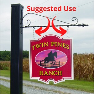 May include: A red and white sign with the text "Twin Pines Ranch" and a silhouette of a horse jumping a fence. The sign is hanging from a black metal bracket.