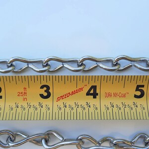 May include: A close-up of a silver chain measured with a yellow tape measure. The tape measure shows markings for inches and feet. The chain is 7 feet long.