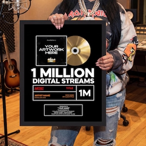 May include: A framed gold record award with the text "1 MILLION DIGITAL STREAMS." The award includes space for the artist's name, album title, and artwork. The award is held by a person in a recording studio.