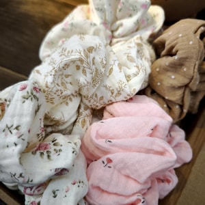 May include: A selection of fabric scrunchies in different colours and patterns. The scrunchies include white with gold floral, white with pink floral, pink with small red flowers, and brown with white polka dots.